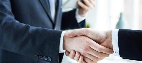 Foto ravvicinata di una stretta di mano fra due uomini che indossano un completo elegante in un ufficio