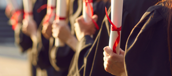 una fila di laureati di spalle con toga e in mano diploma