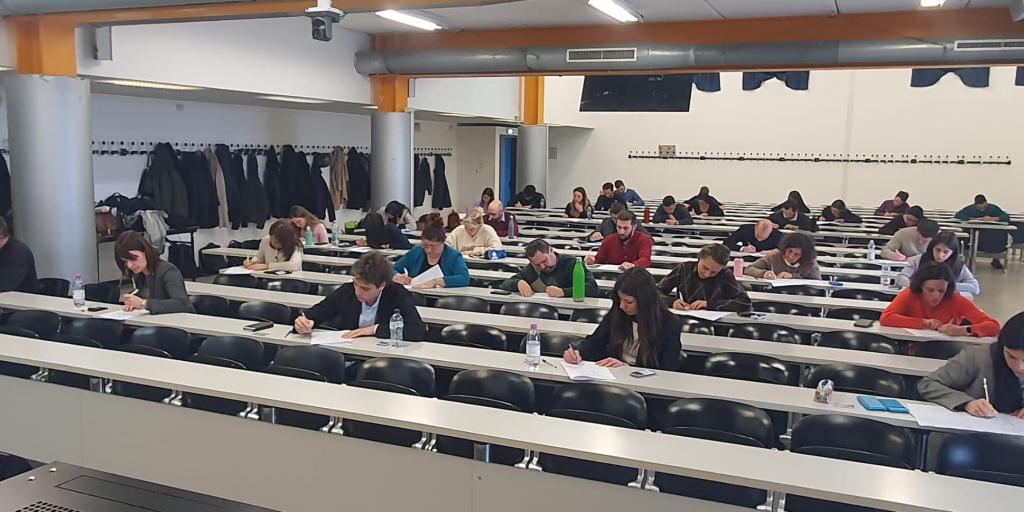 aula universitaria moderna, una decina di studenti e studentesse stanno scrivendo seduti alle loro postazioni